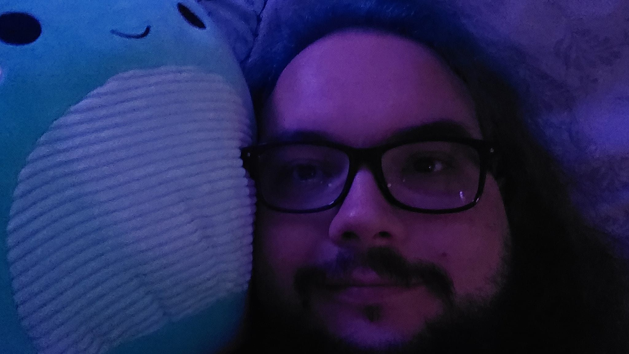 A man with green hair laying with Nessie, a Squishmallows